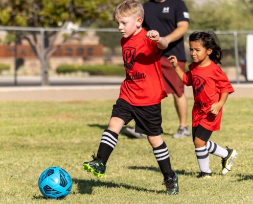 Two young Paladin players chasing a soccer ball.